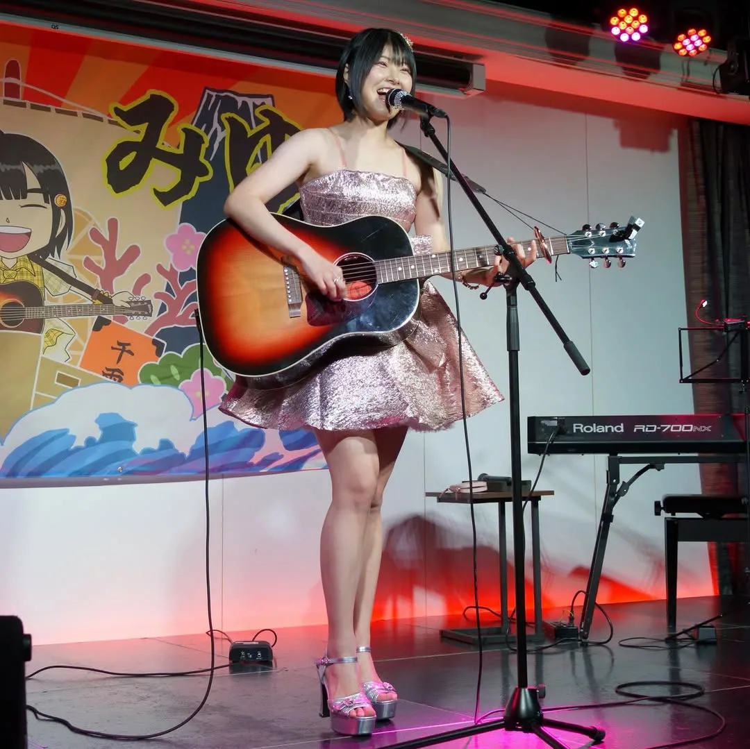 ピンクの衣装でギターを演奏する小松みゆ